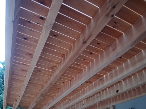 Drewniana konstrukcja dachu z widocznymi belkami i deskami, jasne drewno z naturalnymi sękami, widok od dołu.