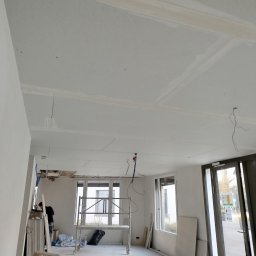 Gromix - Wnętrze w trakcie prac wykończeniowych: sufit z płyt gipsowo-kartonowych z widocznymi łączeniami szpachlowanymi, częściowo odsłonięta konstrukcja stropu, drabina i rusztowanie w pomieszczeniu...