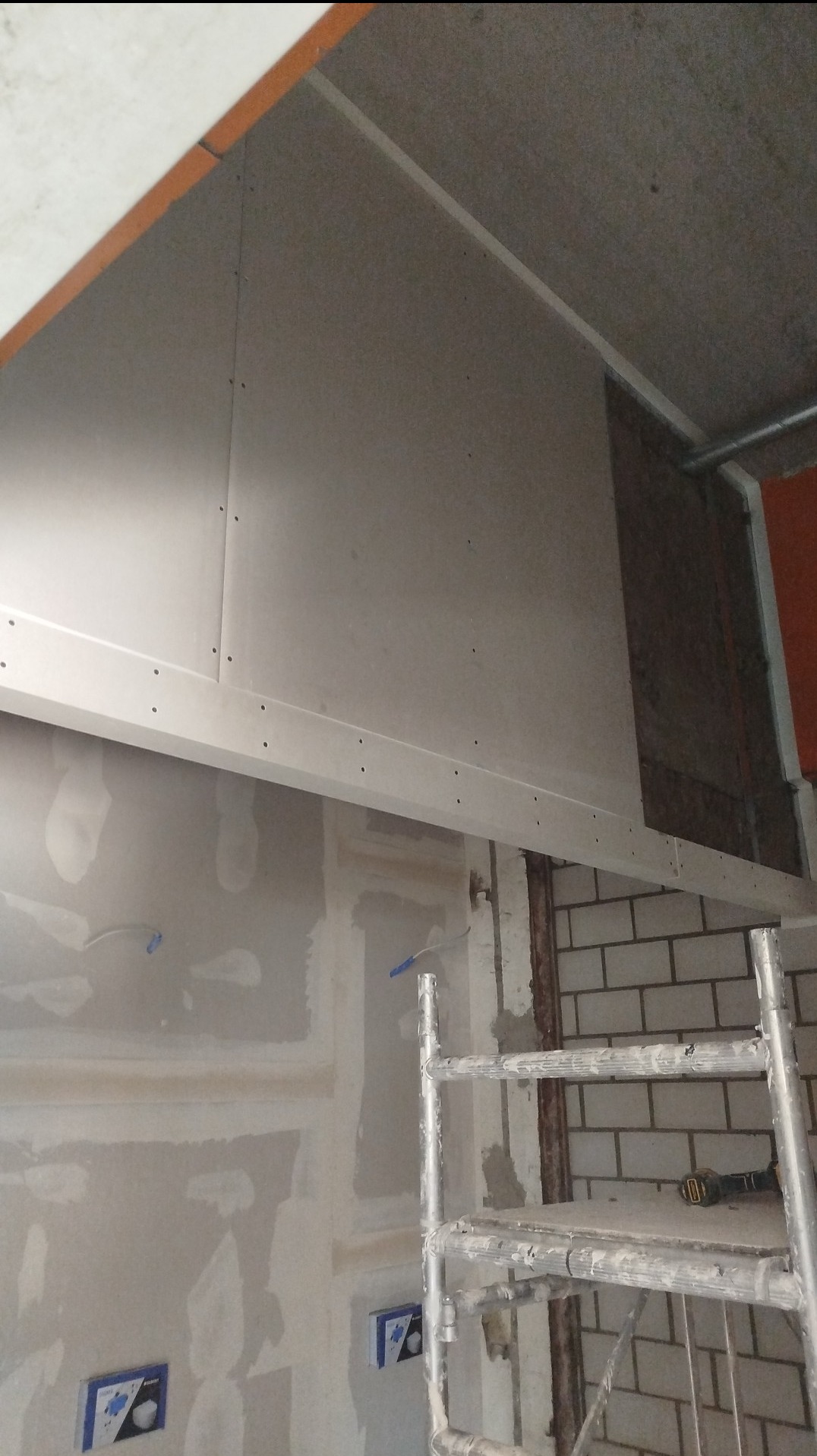 Montaż płyty karton gips na suficie, widoczna drabina, ściana z cegły i fragment instalacji elektrycznej.