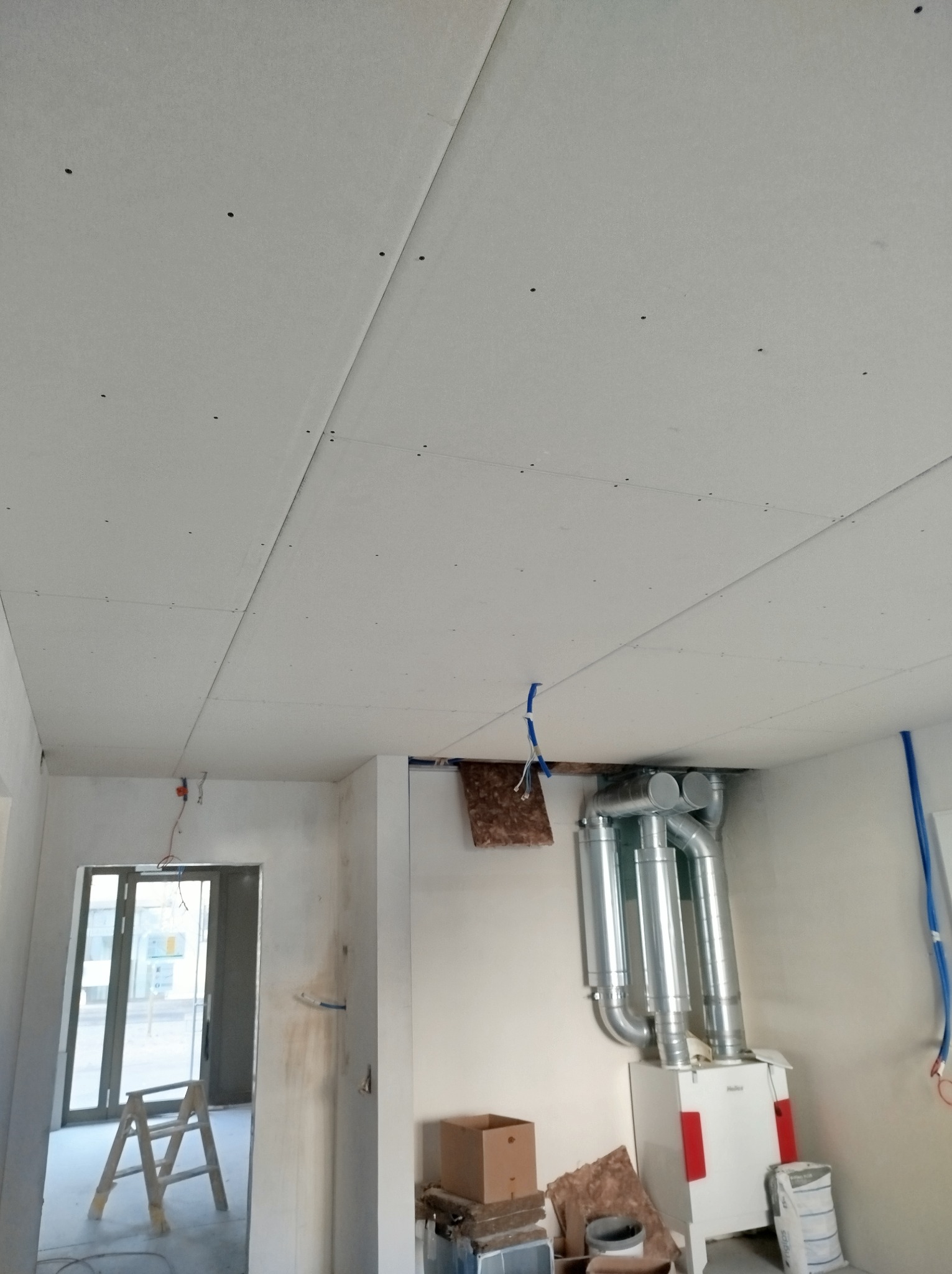 Montaż sufitu podwieszanego z płyt gipsowo-kartonowych w pomieszczeniu z widoczną instalacją wentylacyjną i drabiną w tle.