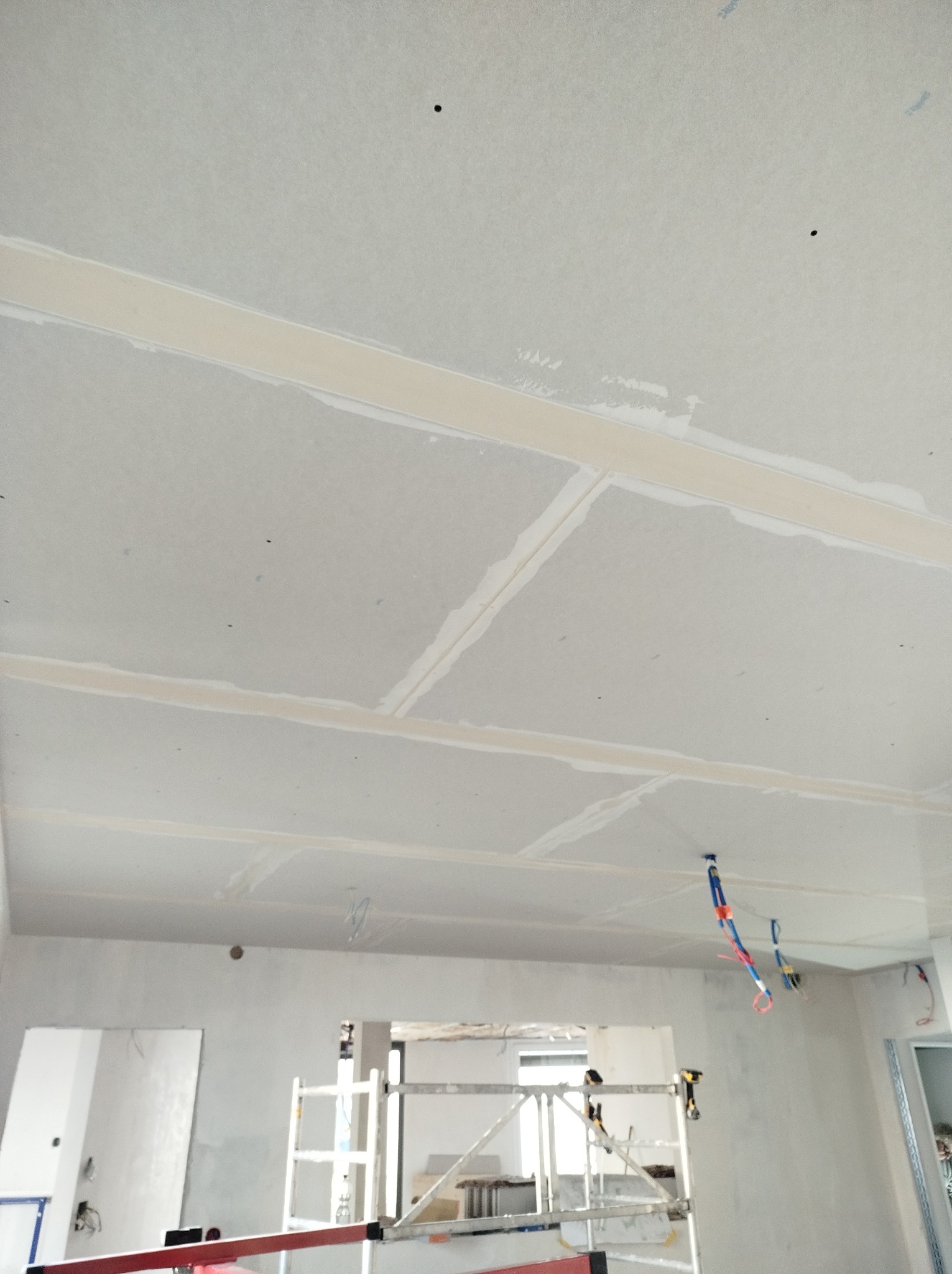 Sufit z płyt kartonowo-gipsowych, widoczne łączenia szpachlowane, w tle rusztowanie i wystające przewody elektryczne.