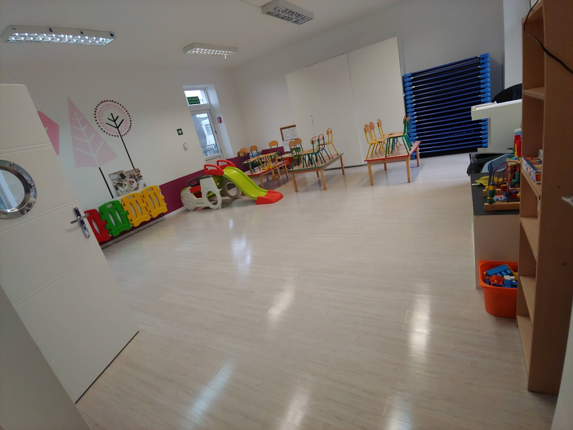 Wnętrze sali przedszkolnej z meblami i zabawkami, widok na czystą podłogę i pomalowane ściany.