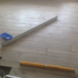 Układanie podłogi z płytek imitujących drewno, widoczne poziomice, krzyżyki dystansowe i niezapełnione fugi.