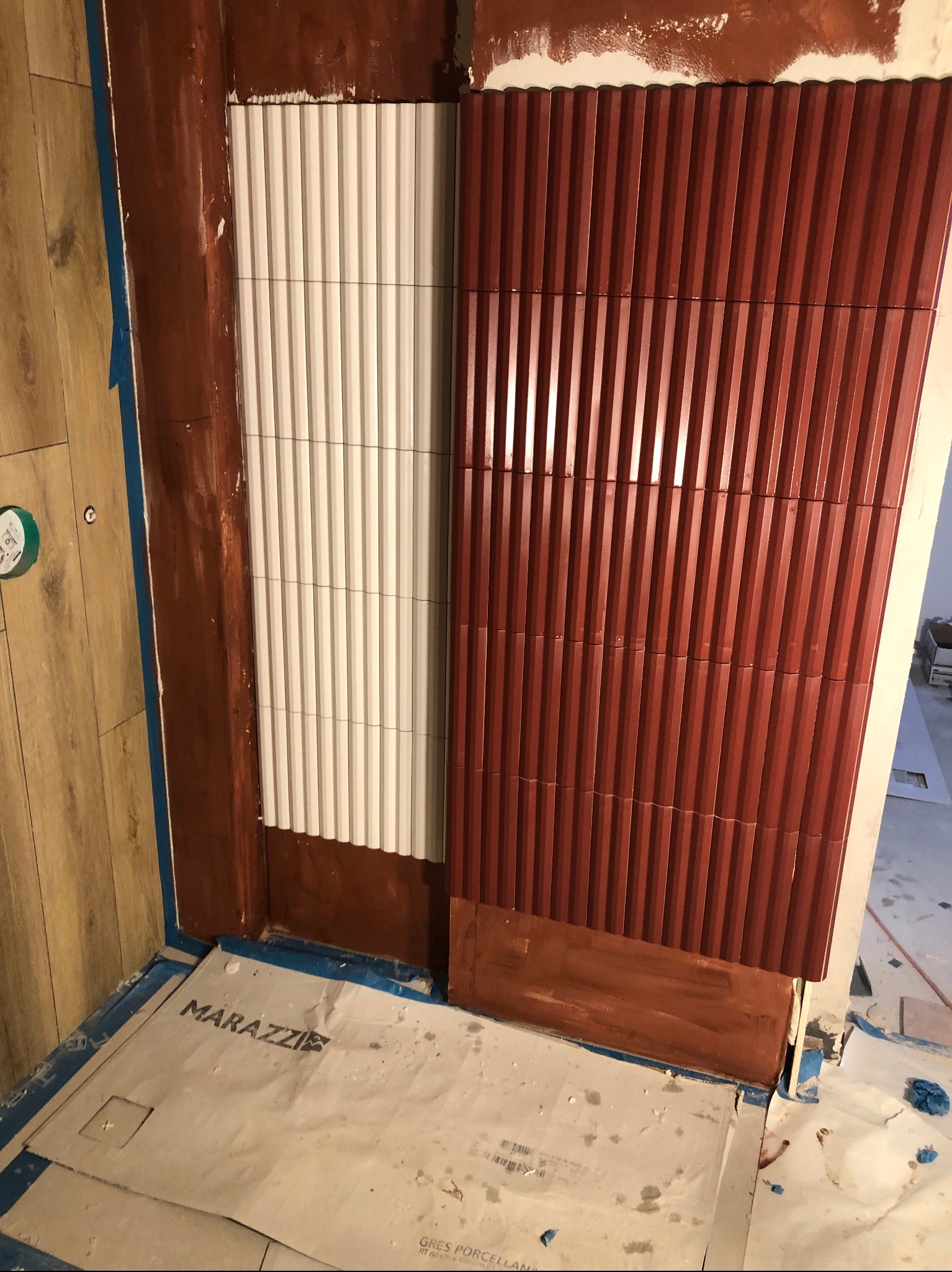 Montaż dekoracyjnych paneli ściennych w odcieniach bieli i terakoty, widoczne zabezpieczenia podłogi kartonem z logo producenta płytek Marazzi.