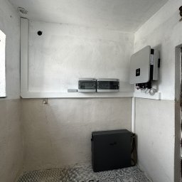 AURUM Energia - Montaż domowej instalacji z magazynem energii Fox w pomieszczeniu z wzorzystą podłogą w Łobudzicach, widoczne skrzynki bezpiecznikowe i inwerter na ścianie.