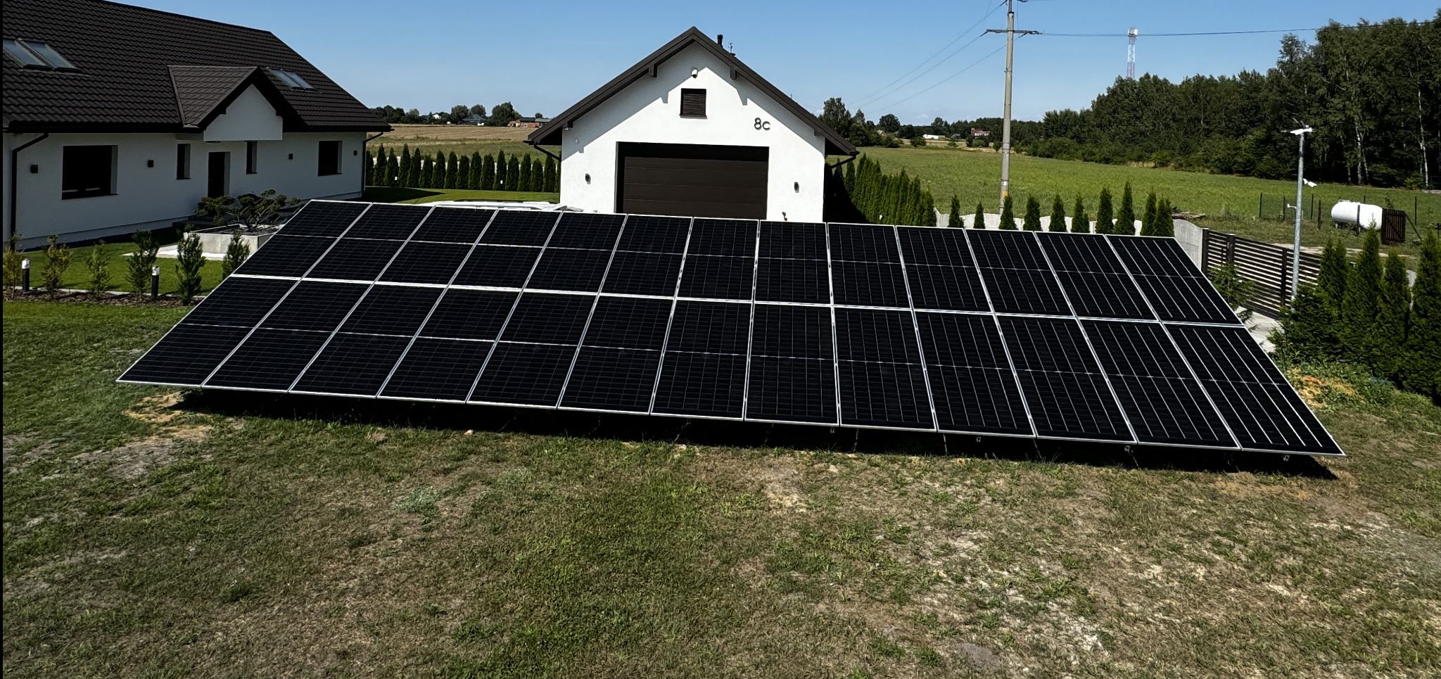Instalacja paneli słonecznych na trawniku przed domem jednorodzinnym z garażem, widok z niskiej perspektywy.