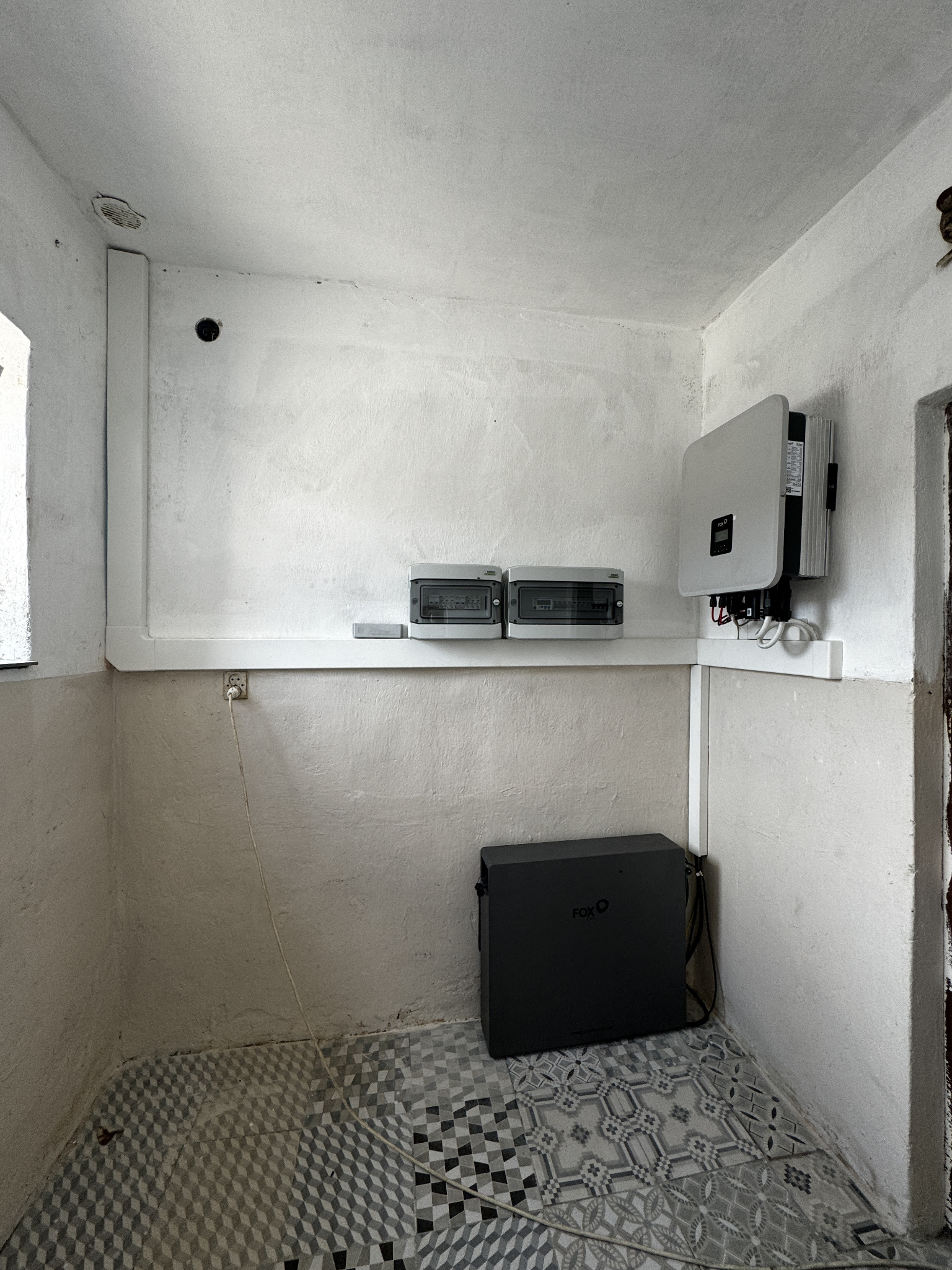 Montaż domowej instalacji z magazynem energii Fox w pomieszczeniu z wzorzystą podłogą w Łobudzicach, widoczne skrzynki bezpiecznikowe i inwerter na ścianie.