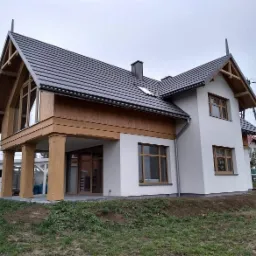 Nowoczesny dom jednorodzinny z grafitową dachówką i drewnianymi elementami wykończeniowymi w Brzesku. Widok z zewnątrz, jesienna sceneria.