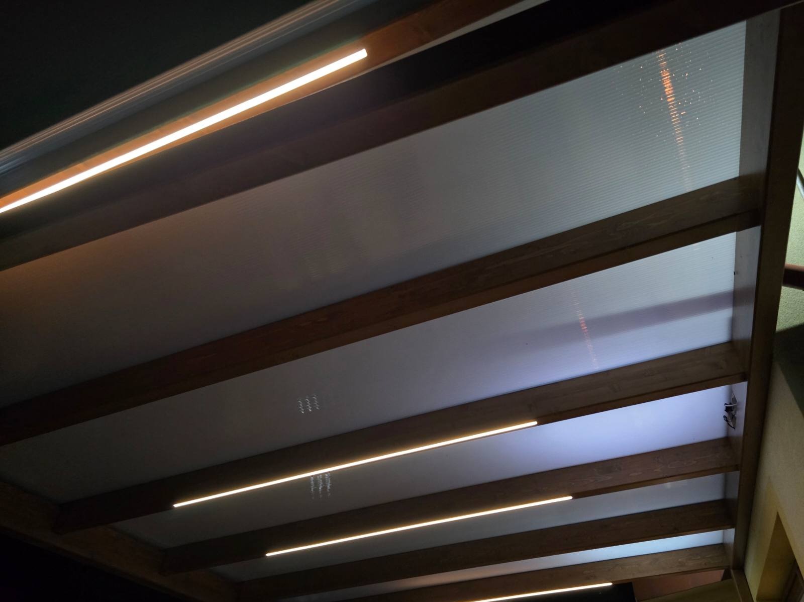 Pergola z drewnianą konstrukcją i oświetleniem LED wbudowanym w belki, widok od dołu.