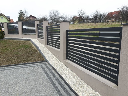 Nowoczesne, poziome ogrodzenie panelowe w kolorze antracytowym z betonowymi słupkami, oddzielające posesję od trawnika i ścieżki z białego kamienia.