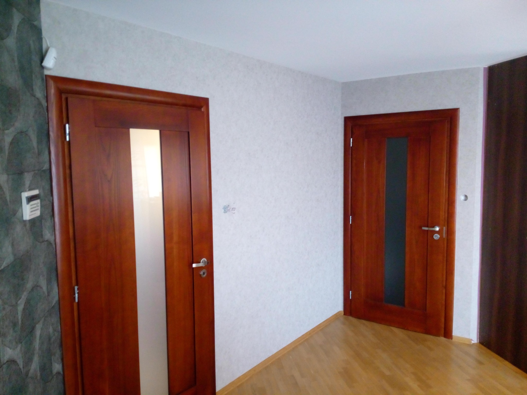 Dwa dębowe, wewnętrzne drzwi z szybami, zamontowane w pokoju z jasnymi ścianami pokrytymi tapetą o delikatnym wzorze i drewnianą podłogą.