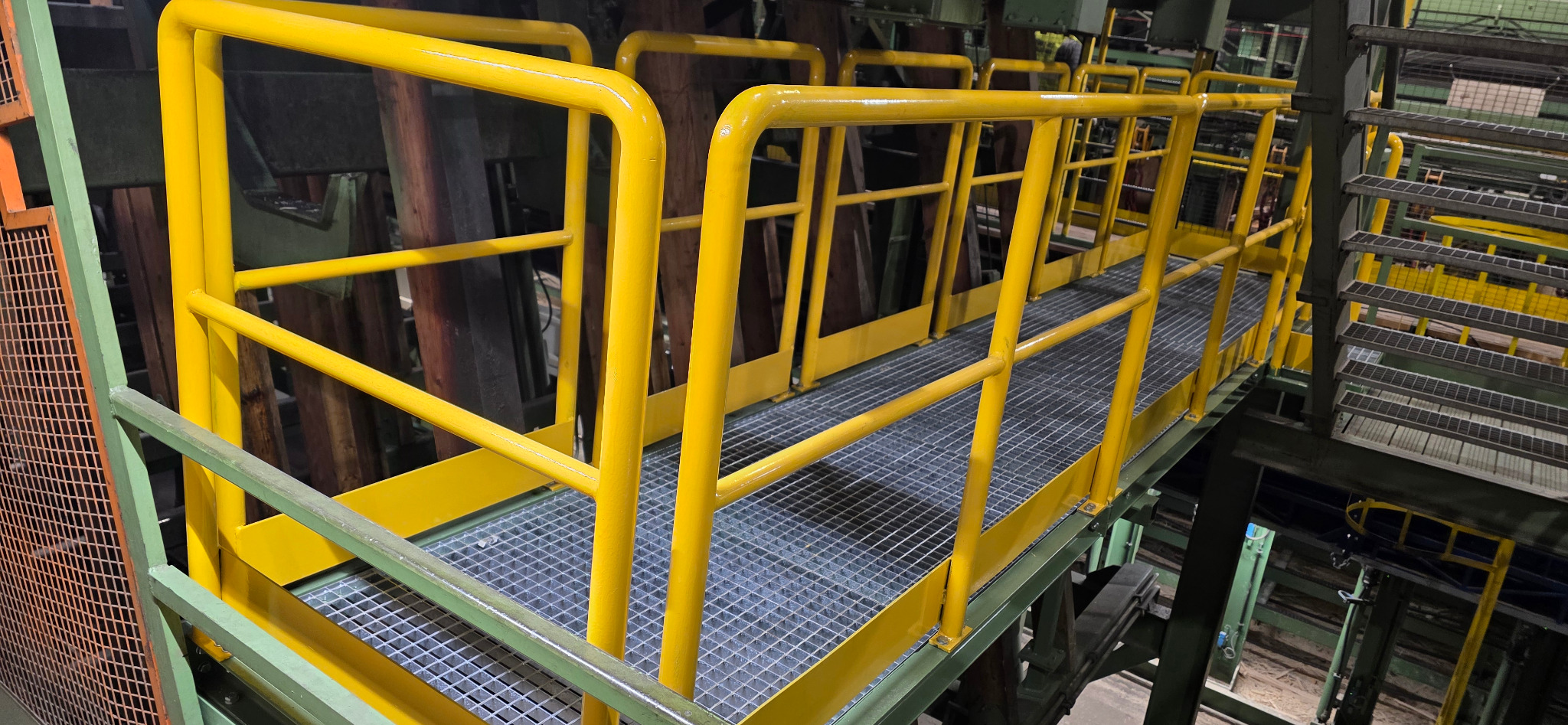 Metalowa konstrukcja pomostu z żółtymi barierkami i kratą podłogową, element infrastruktury przemysłowej, spawana konstrukcja, widok z perspektywy.