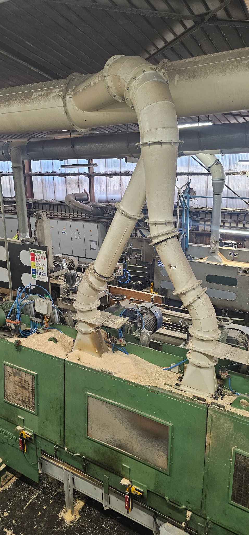 System odciągu trocin z maszyny do obróbki drewna. Widoczne rury wentylacyjne, silniki i elementy sterujące. Trociny na maszynie.