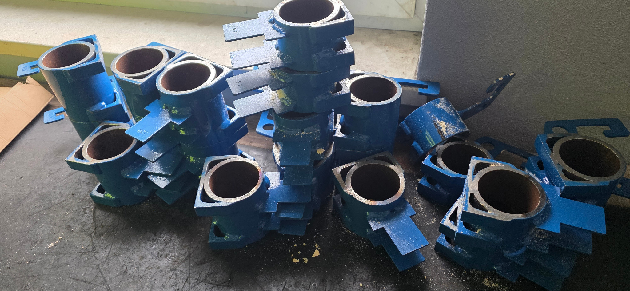 Stos niebieskich, metalowych elementów konstrukcyjnych z otworem, prawdopodobnie po obróbce. Widoczne ślady farby i niedoskonałości wykończenia.