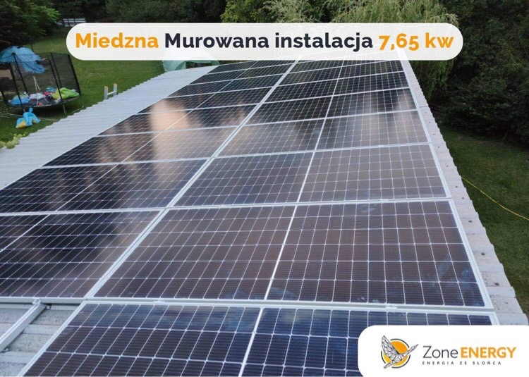 Panel słoneczny o mocy 7,65 kW zamontowany na dachu domu, widok z góry, z logo firmy w prawym dolnym rogu.