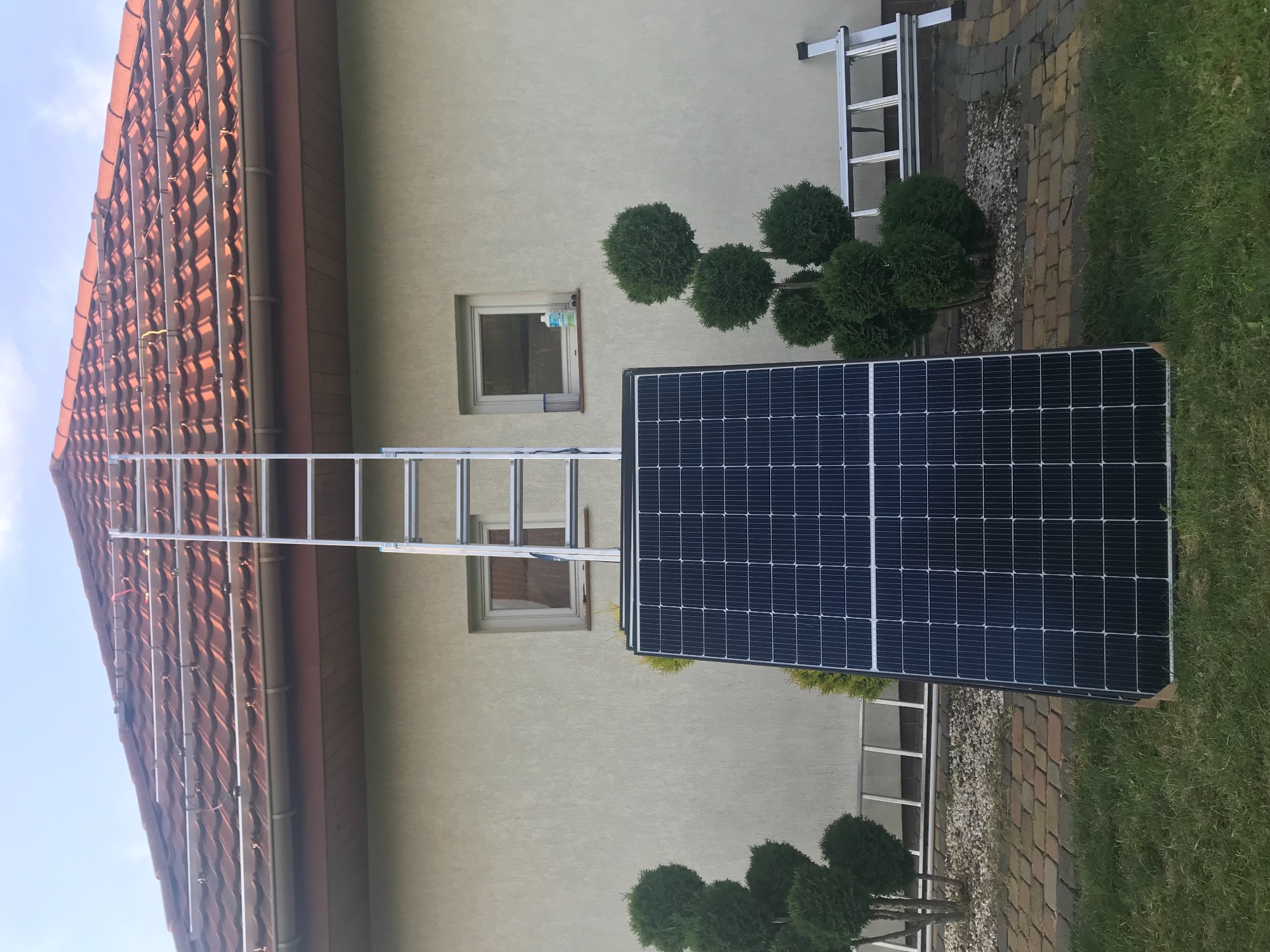 Panel słoneczny oparty o ścianę domu z drabiną opartą o dach, przygotowany do montażu.