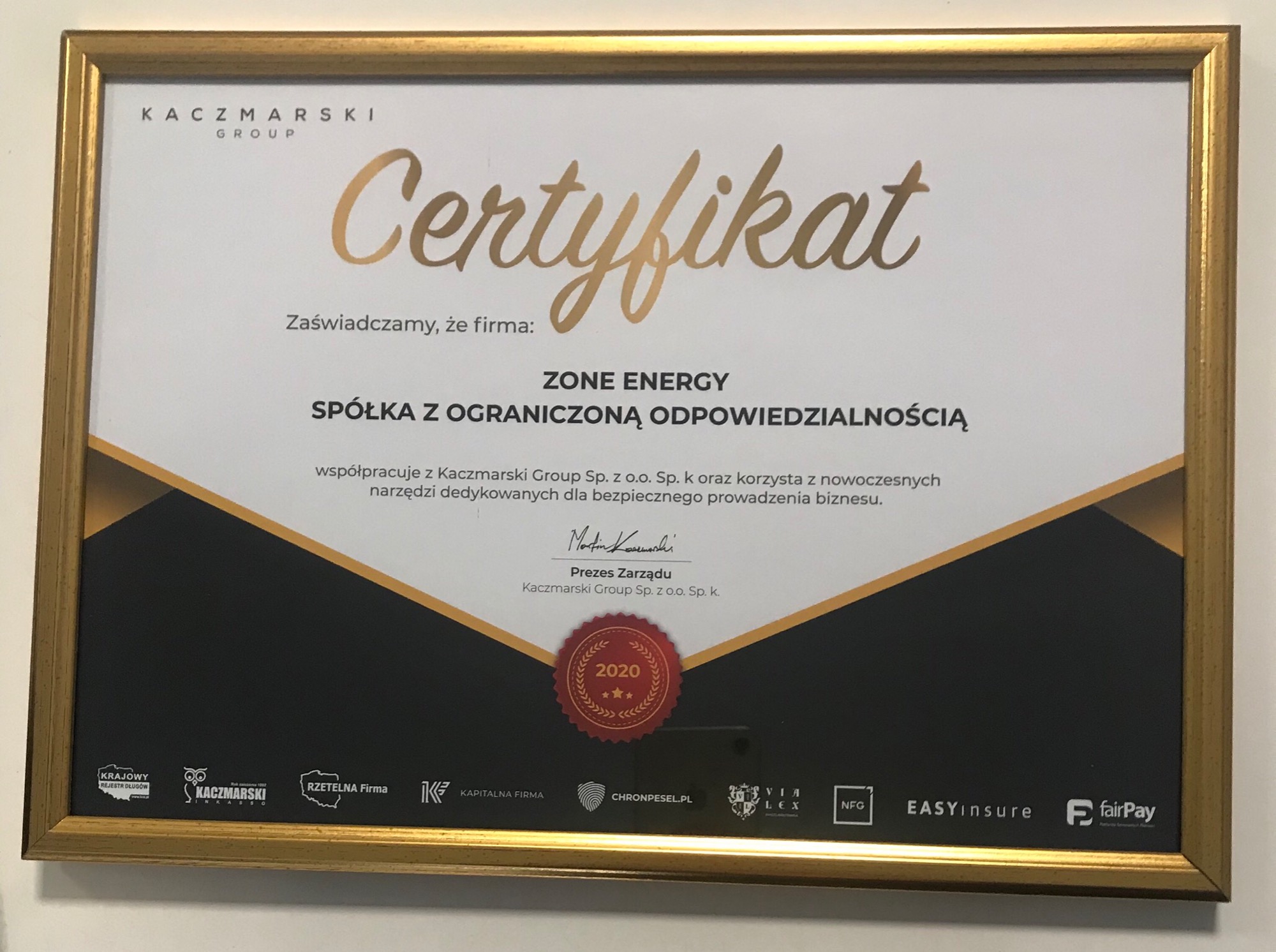Oprawiony w złotą ramkę certyfikat firmy Kaczmarski Group dla ZONE ENERGY Spółka z ograniczoną odpowiedzialnością, potwierdzający współpracę i korzystanie z nowoczesnych narzędzi biznesowych,...