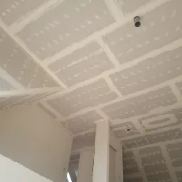 Sufit i ściany wykończone płytami kartonowo-gipsowymi, z widocznymi łączeniami wypełnionymi szpachlą, przygotowane do malowania. Widoczny fragment instalacji wentylacyjnej w suficie.