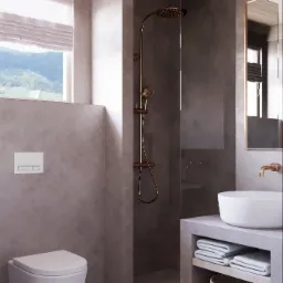 Nowoczesna łazienka z szarą ścianą, wiszącą toaletą, kabiną prysznicową typu walk-in z miedzianą armaturą, białą umywalką nablatową, ręcznikami i koszem wiklinowym, z widokiem na góry za oknem.