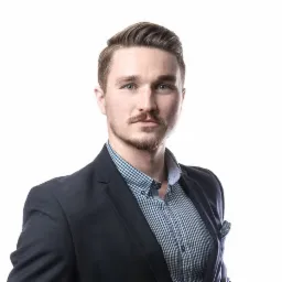 Portret biznesowy mężczyzny z lekkim uśmiechem, w niebieskiej koszuli w kratę i granatowej marynarce na białym tle.