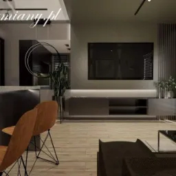 Nowoczesny salon z drewnianą podłogą, szarą ścianą z telewizorem, minimalistyczną szafką RTV z podświetleniem LED, roślinami w srebrnych donicach i brązowymi krzesłami barowymi na metalowych nogach.