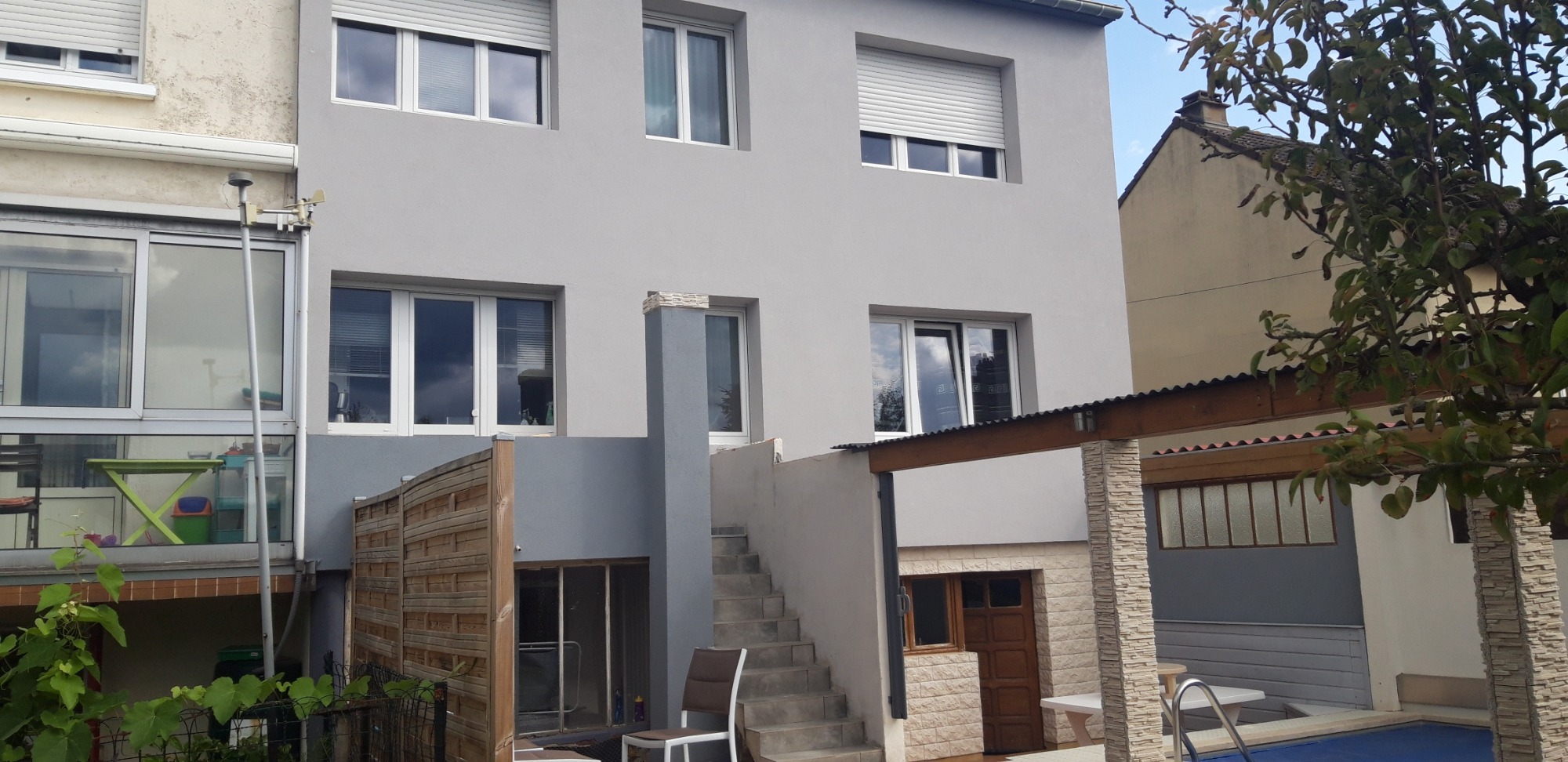 Dwupiętrowy budynek po remoncie z szarą elewacją, widoczne okna z roletami, schody zewnętrzne i częściowo zadaszony taras z kolumnami wykończonymi kamieniem.
