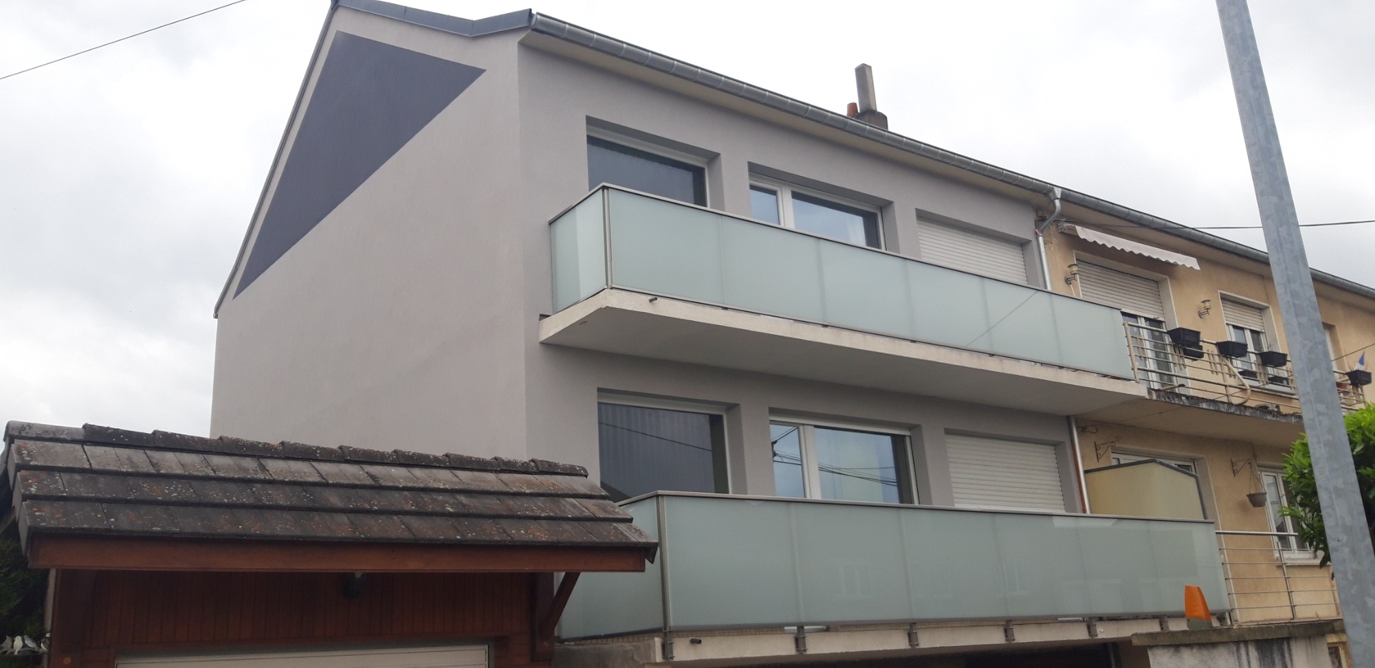 Odnowiona elewacja dwupiętrowego budynku w Kielcach, z szarą fasadą i balkonami z mlecznego szkła, widoczny fragment dachu garażu z przodu.