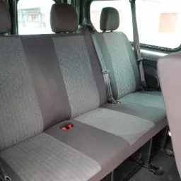 Wnętrze busa: trzyosobowa tylna kanapa z szarą tapicerką w geometryczny wzór, widoczne pasy bezpieczeństwa i uchwyty na napoje.