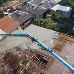 Betonowanie stropu budynku wielorodzinnego z użyciem pompy do betonu, widok z góry na konstrukcję zbrojeniową i robotników w kaskach.