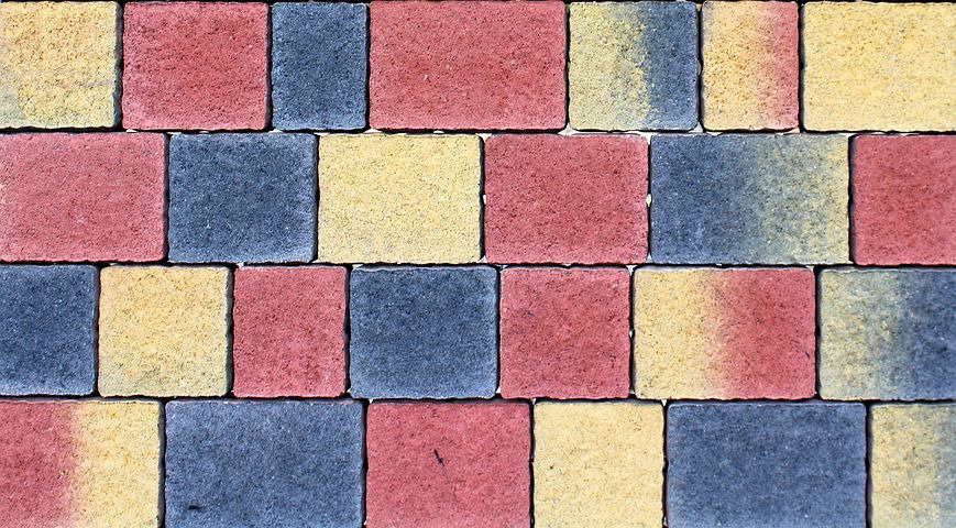 Kolorowa kostka brukowa ułożona w regularny wzór z dominacją odcieni czerwieni, żółci i szarości, widok z góry.