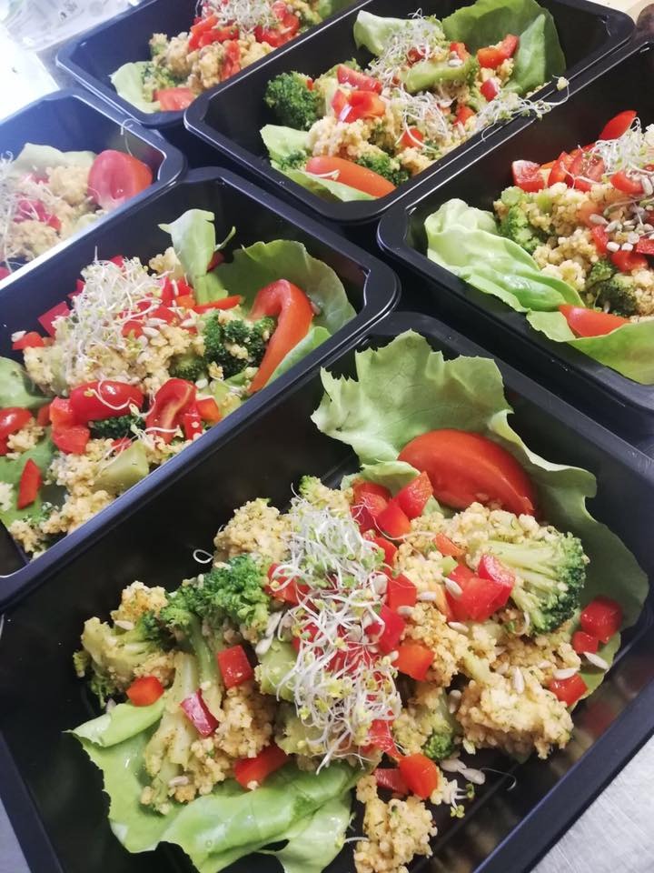 Gotowe porcje sałatki warzywnej z brokułami, czerwoną papryką i kiełkami, ułożone na liściach sałaty w czarnych, plastikowych pojemnikach.