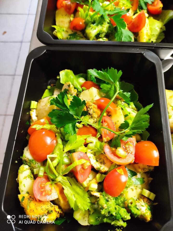 Dwa czarne pojemniki z dietetyczną sałatką warzywną z pomidorkami koktajlowymi i zieloną pietruszką, gotowe do transportu.