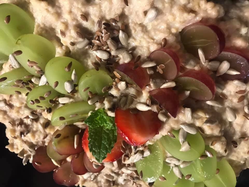 Zbliżenie na owsiankę udekorowaną zielonymi i czerwonymi winogronami, truskawkami, miętą i ziarnami słonecznika oraz lnu.