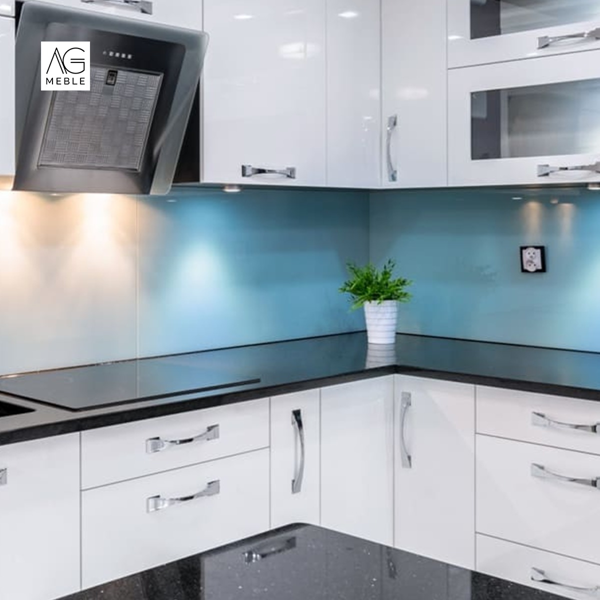 Biała, nowoczesna kuchnia z błyszczącymi frontami, czarnym blatem z drobinkami, niebieskim panelem nad blatem i metalowym okapem; na blacie doniczka z zieloną rośliną.