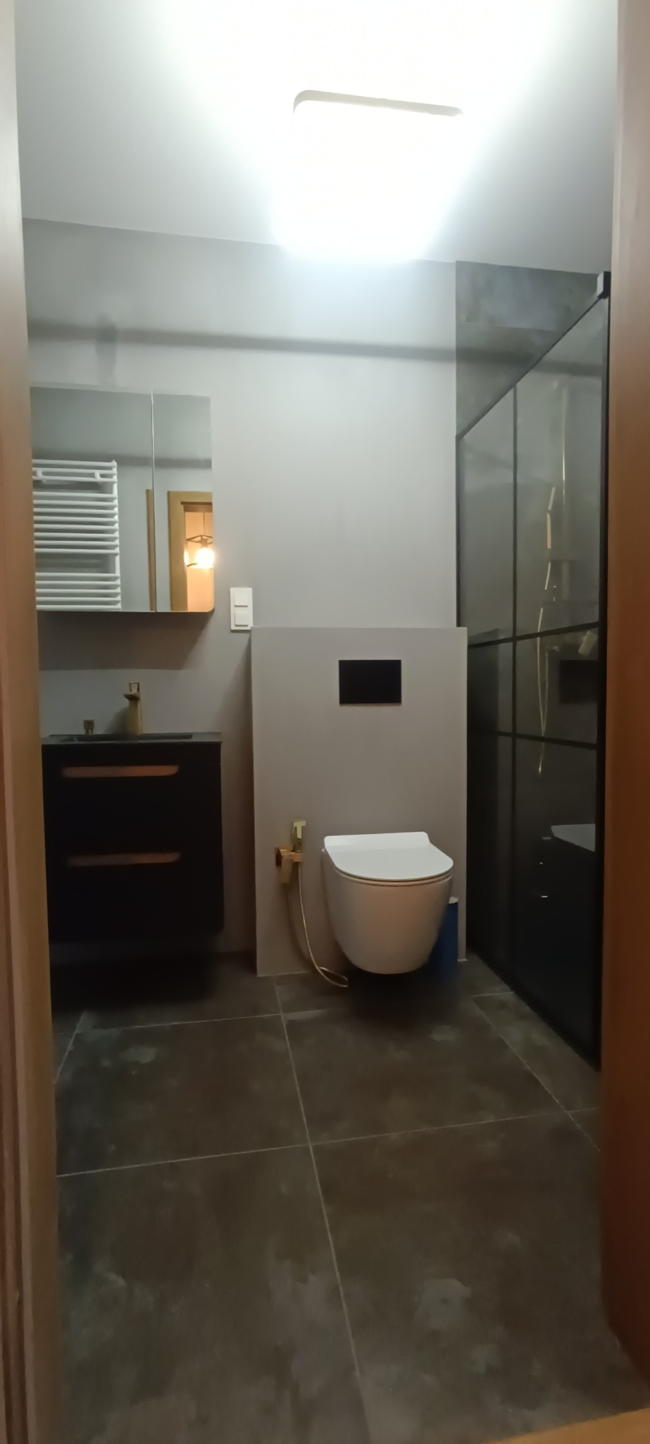 Nowoczesna łazienka we Wrocławiu z podwieszaną toaletą z bidetką w kolorze złotym, czarną szafką pod umywalką i kabiną prysznicową z czarnymi ramami.