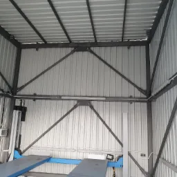 Wnętrze metalowej konstrukcji hali z widocznym podnośnikiem samochodowym, oświetleniem i instalacją elektryczną na ścianach z blachy trapezowej.