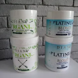 Cztery białe pojemniki z maskami do włosów marki Dianv Organics i Dianv Platinum Blond na tle szarej ściany z cegieł, widoczne opisy Neutralizing Mask, Reconstructor B-Tox i Toning Mask.