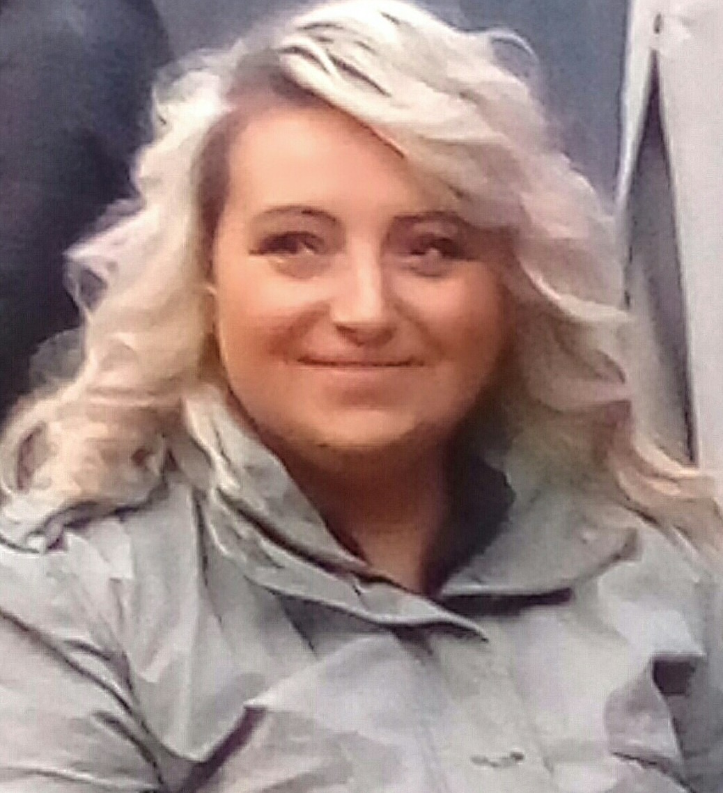 Portret uśmiechniętej kobiety z pofalowanymi, platynowymi włosami po koloryzacji, widoczny zarys ramion w szarej kurtce.