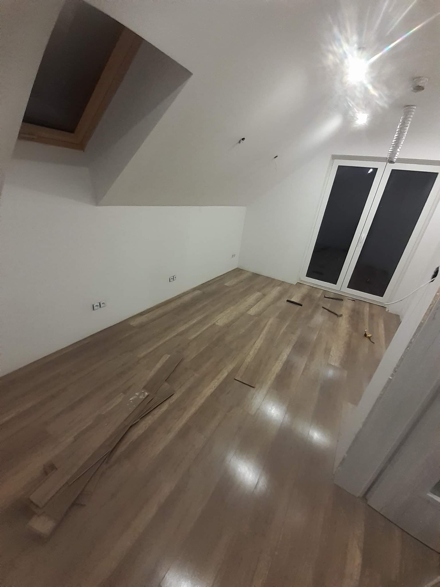 Poddasze z oknem dachowym i częściowo ułożonym parkietem z widocznymi narzędziami i resztkami paneli.