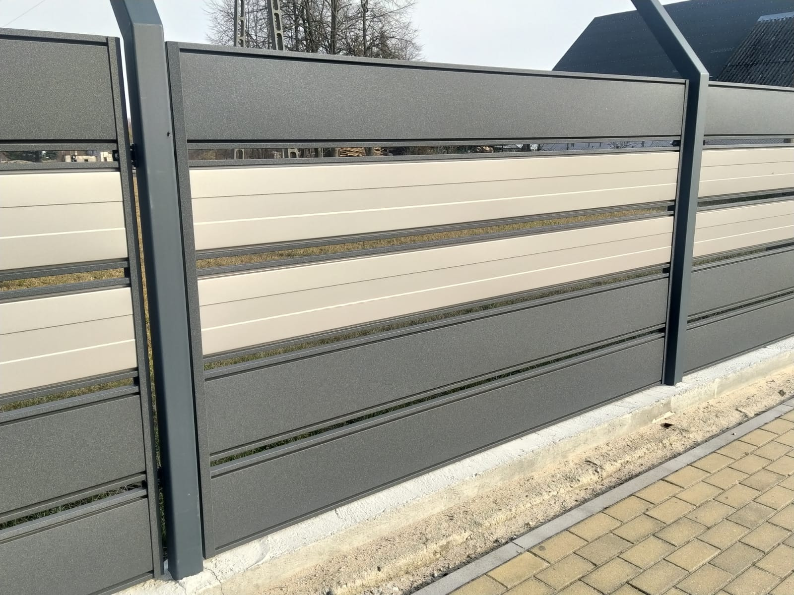 Nowoczesne ogrodzenie z paneli w odcieniach szarości i beżu, zamontowane w Kazanowie, z widocznymi poziomymi szczelinami między panelami i betonową podmurówką.