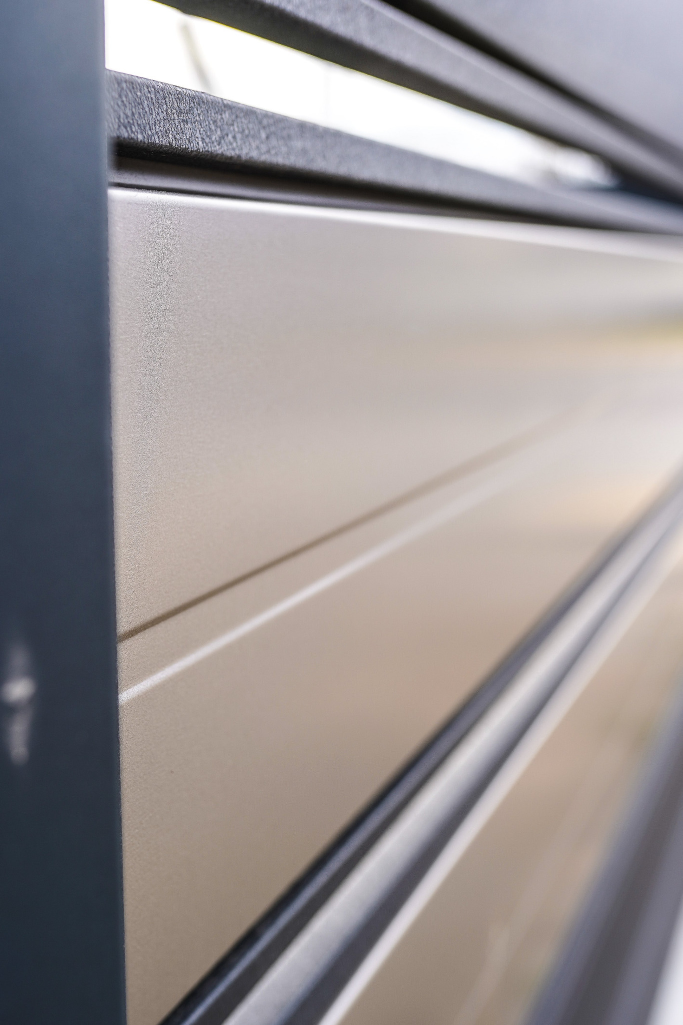 Detal pionowego ujęcia fragmentu beżowego ogrodzenia panelowego z bliska, widoczna faktura paneli i ciemnoszara rama.