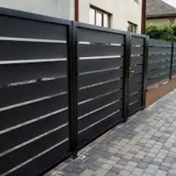 Czarna, nowoczesna brama wjazdowa z poziomymi, metalowymi panelami i wąskimi prześwitami, na tle kostki brukowej i budynku mieszkalnego.