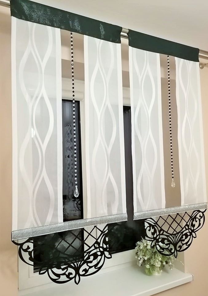 Delikatne, białe zasłony z falistym wzorem, ozdobione czarnymi koralikami i srebrną taśmą, wykończone dekoracyjną, czarną aplikacją na parapecie okiennym, z bukiecikiem białych kwiatów.