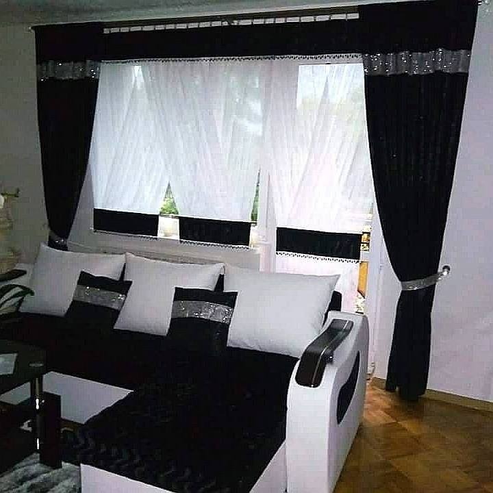 Salon z czarno-białymi zasłonami z woalu i aksamitu, dekorowanymi srebrnymi akcentami, dopasowanymi do poduszek na kanapie.