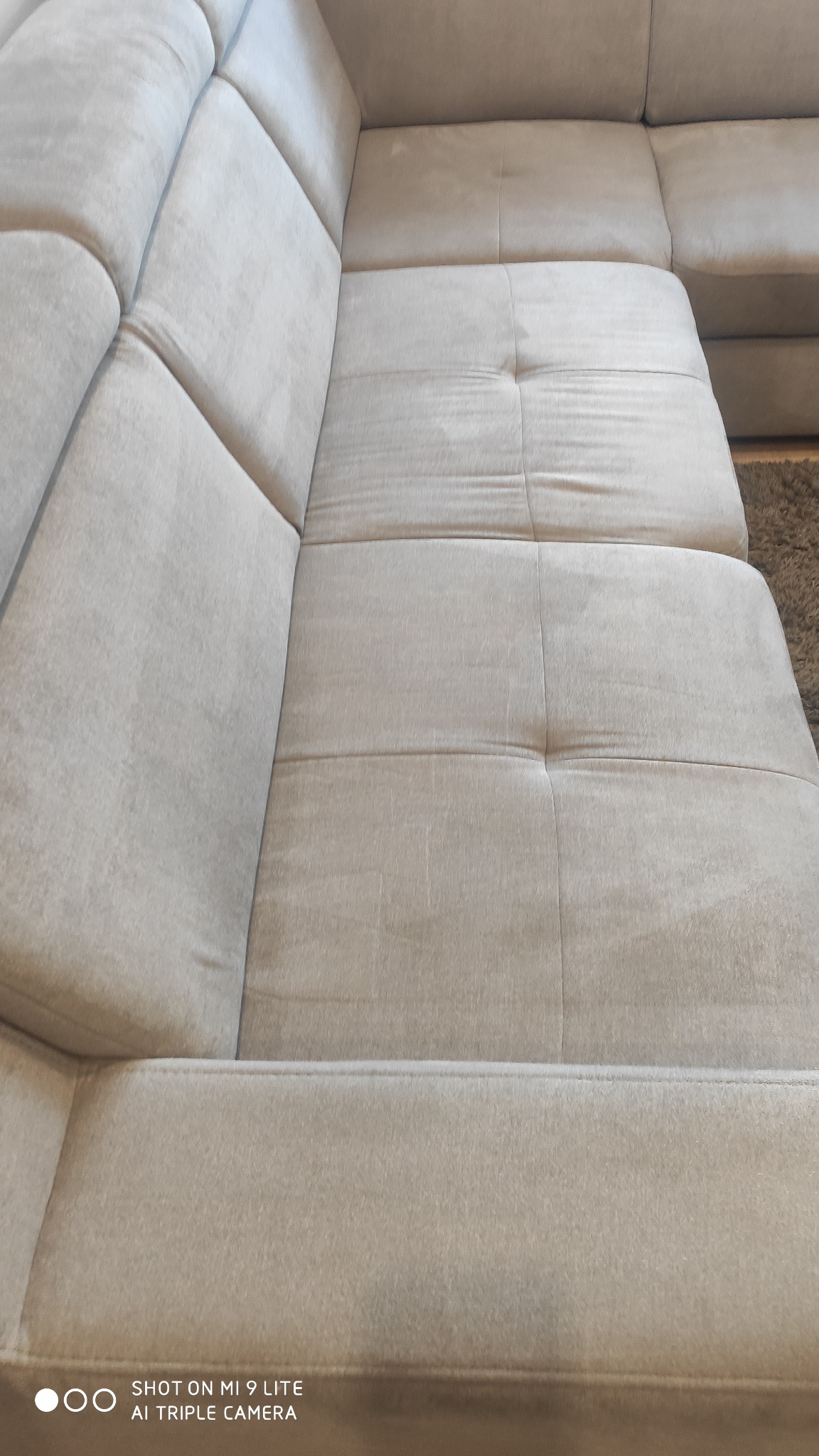 Fragment beżowej, modułowej sofy z miękkim, pluszowym obiciem, widoczny z bliska, z delikatnym cieniowaniem podkreślającym fakturę materiału.