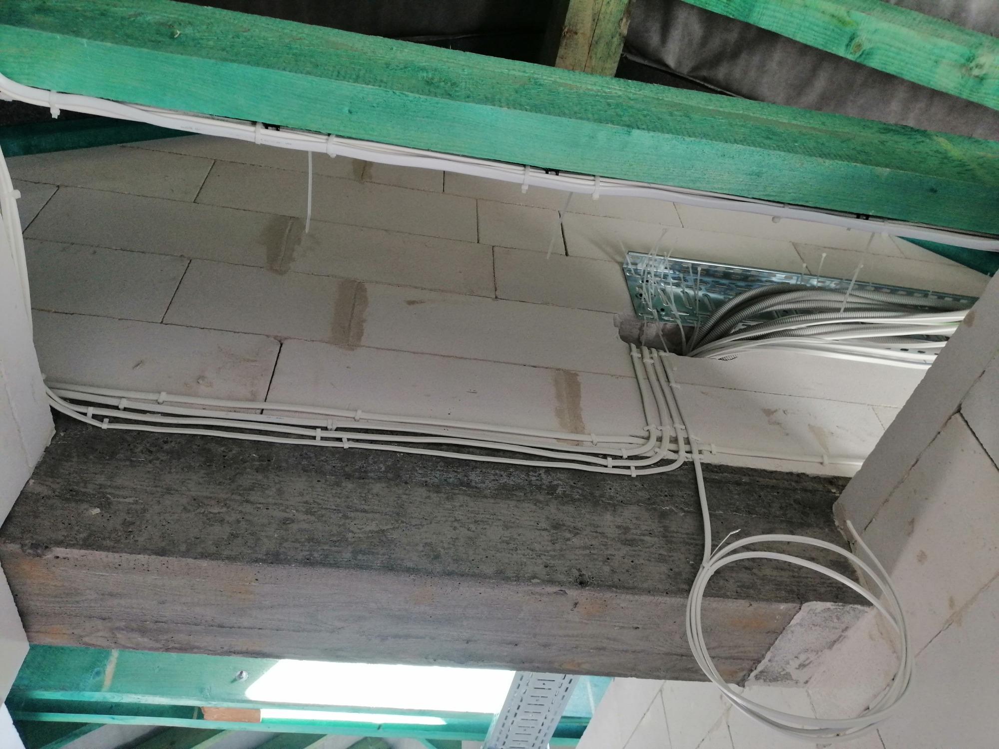 Wewnętrzne okablowanie elektryczne w nowym budynku, kable zabezpieczone opaskami zaciskowymi, widoczne elementy konstrukcji dachu i ściany z betonu komórkowego.