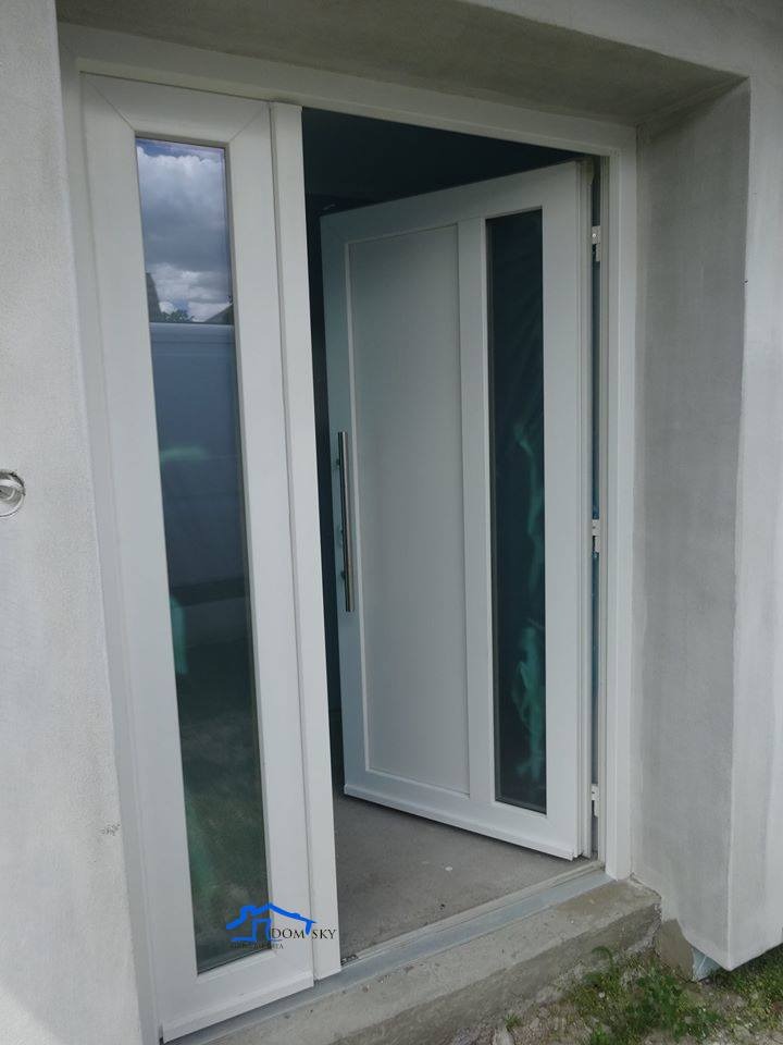 Białe drzwi wejściowe z szybą, częściowo otwarte na zewnątrz, widoczne z bliska, z logo firmy w lewym dolnym rogu.