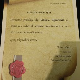 Damian Mlynarczyk - Uroczysty list gratulacyjny dla Damiana Młynarczyka za wybitne wyniki sprzedażowe w sieci Metrohouse, opatrzony czerwoną lakową pieczęcią i podpisem Dyrektora Sprzedaży Beaty Dec.