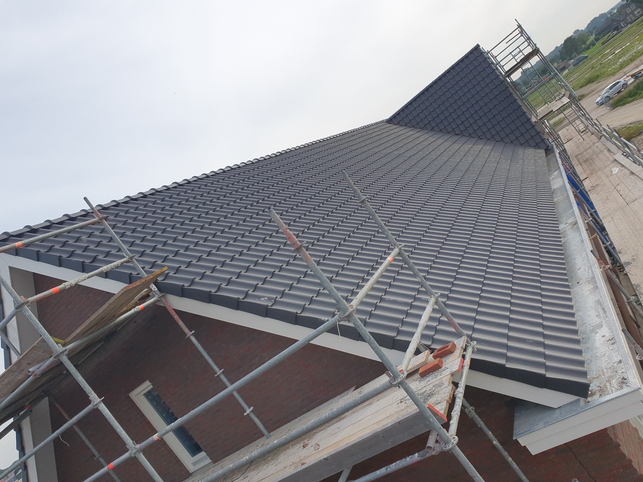 Nowy dach z ciemnoszarej dachówki ceramicznej, widok z góry z rusztowaniem w tle, budynek w trakcie wykończenia.