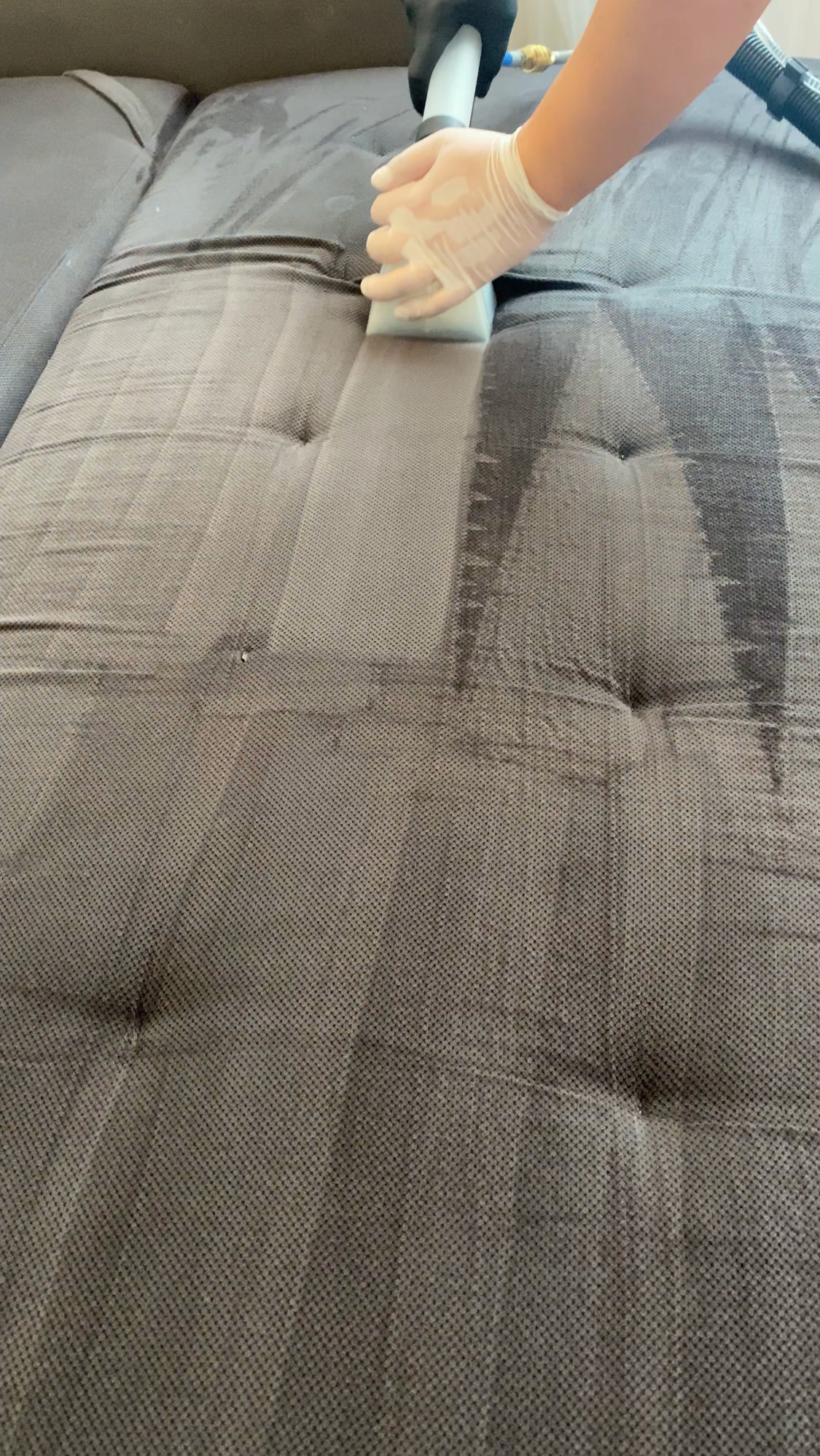 Czyszczenie tapicerki sofy za pomocą odkurzacza piorącego; widoczny efekt czyszczenia, ciemniejszy pas po prawej stronie.